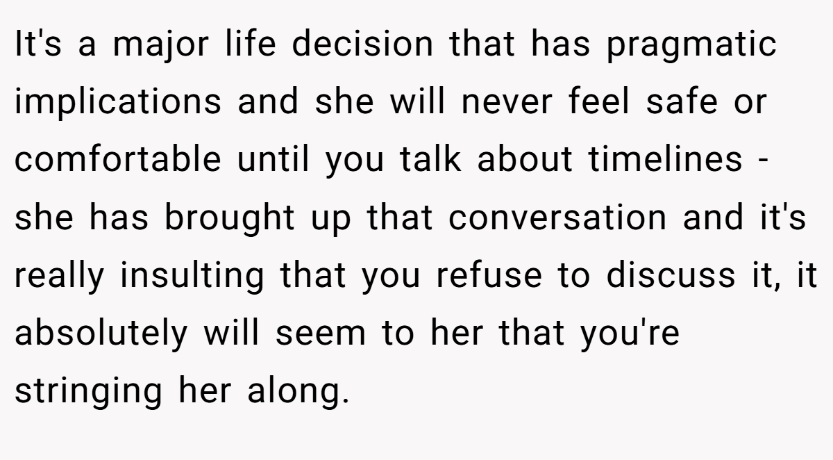 It's a major life decision that has pragmatic implications and she will never feel safe or comfortable until you talk about timelines - she has brought up that conversation and it's really insulting that you refuse to discuss it, it absolutely will seem to her that you're stringing her along.