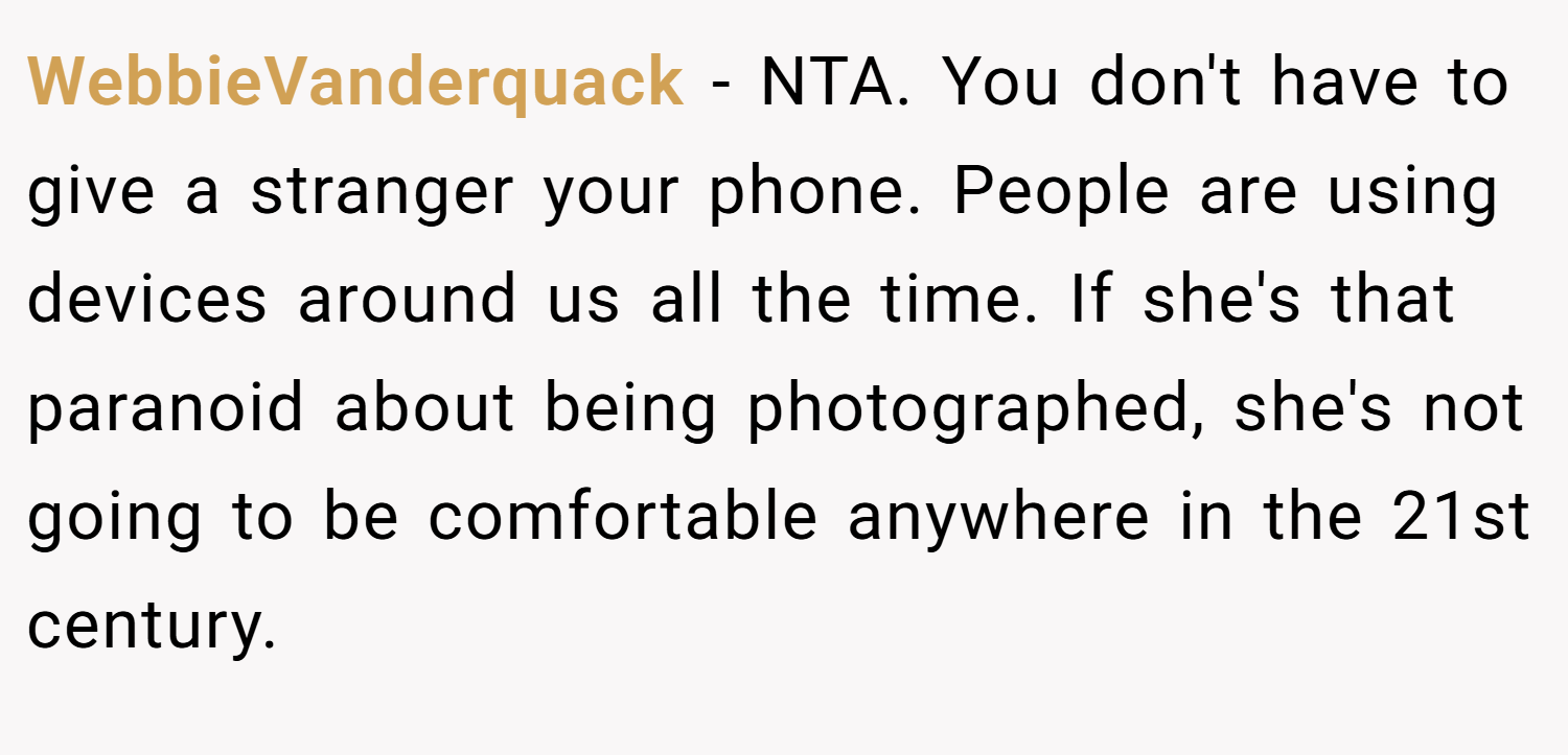 WebbieVanderquack − NTA. You don't have to give a stranger your phone. People are using devices around us all the time. If she's that paranoid about being photographed, she's not going to be comfortable anywhere in the 21st century.