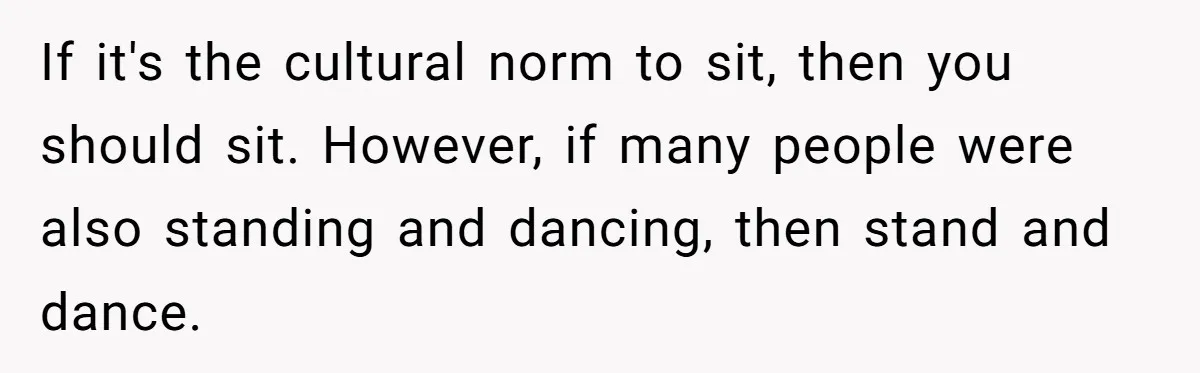 If it's the cultural norm to sit, then you should sit. However, if many people were also standing and dancing, then stand and dance.
