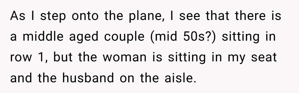 As I step onto the plane, I see that there is a middle aged couple (mid 50s?) sitting in row 1, but the woman is sitting in my seat and...