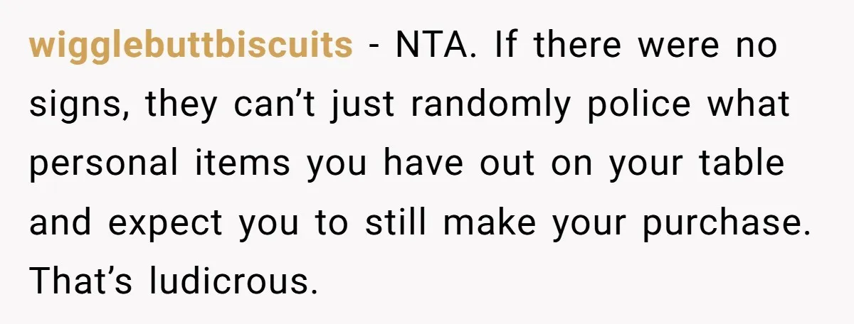 wigglebuttbiscuits − NTA. If there were no signs, they can’t just randomly police what personal items you have out on your table and expect you to still make your purchase....