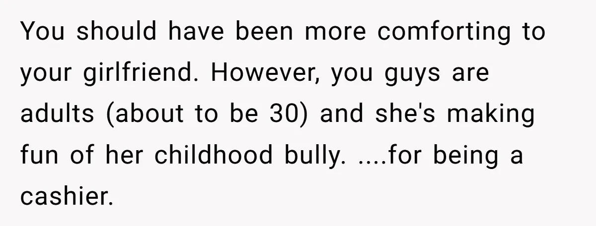 You should have been more comforting to your girlfriend. However, you guys are adults (about to be 30) and she's making fun of her childhood bully. ....for being a cashier.